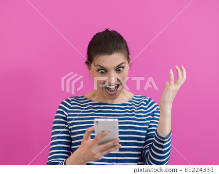 surprised-faced girl looks at her cell phone as she stands in front of a pink background surprised-faced girl looks at her cell phone as she stands in front of a pink background 81224331