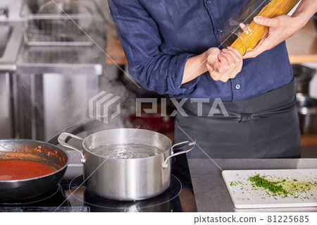 Hand cooking boy image of a young man wearing an apron boiling pasta Hand cooking boy image of a young man wearing an apron boiling pasta 81225685