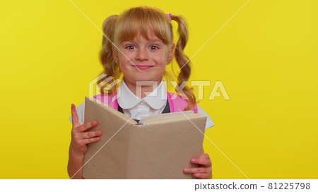Lovely teenage girl kid in school uniform wears pink backpack peeping while hiding behind a book Lovely teenage girl kid in school uniform wears pink backpack peeping while hiding behind a book 81225798