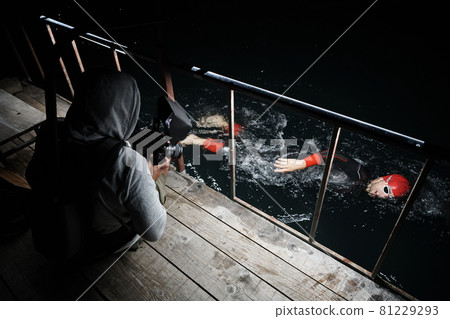 videographer taking action shot of triathlon swimming athlete at night 81229293