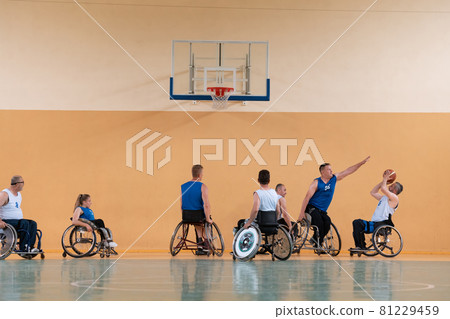 Disabled War veterans mixed race opposing basketball teams in wheelchairs photographed in action while playing an important match in a modern hall.  81229459