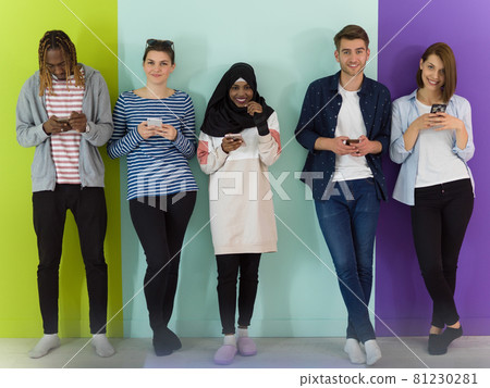 diverse teenagers use mobile devices while posing for a studio photo in front of a pink background 81230281