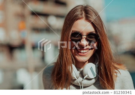 a modern girl with sunglasses walking down the street listens to music in headphones. 81230341