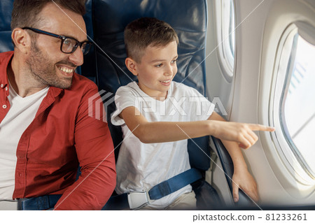 Happy little boy looking out the window, showing something to his father while sitting near the window, traveling by plane together 81233261