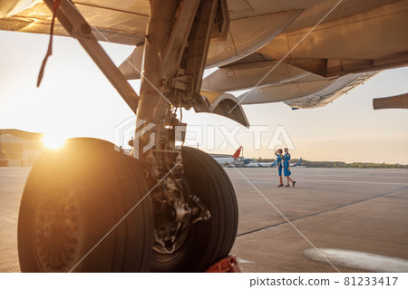 Professional male pilot posing for photoshoot together with two air hostesses in blue uniform, standing in an airport terminal at sunset 81233417