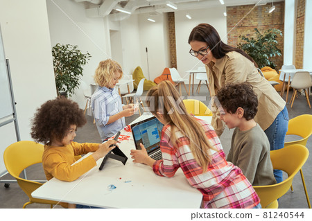 Fun and engaging. Happy children using gadgets during STEM class with young female teacher Fun and engaging. Happy children using gadgets during STEM class with young female teacher 81240544