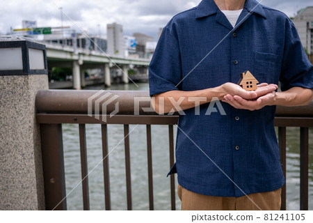 A small house in the palm of a man (urban building background) 81241105