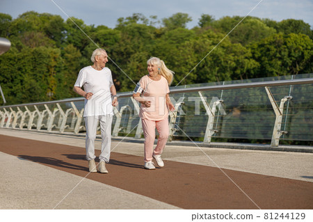 Happy senior man and woman run together along footbridge in summer 81244129