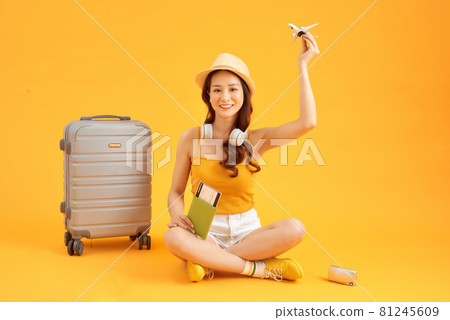 Cute and cheerful woman with a passport in the hands of plane tickets near the gray suitcase 81245609