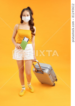 Young woman tourist holding passport wear facial mask posing isolated on yellow orange background Young woman tourist holding passport wear facial mask posing isolated on yellow orange background 81245612