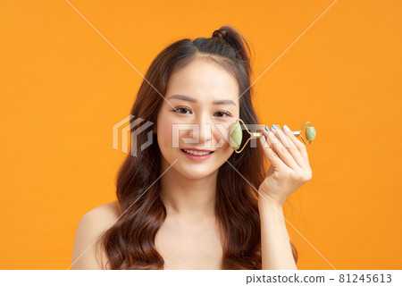 beautiful naked asian girl massaging face with jade roller isolated on yellow orange beautiful naked asian girl massaging face with jade roller isolated on yellow orange 81245613