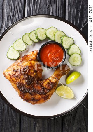 Ayam bakar is an Indonesian and Malaysian dish, consisting of charcoal grilled chicken served with cucumber and hot sauce closeup. Vertical top view Ayam bakar is an Indonesian and Malaysian dish, consisting of charcoal grilled chicken served with cucumber and hot sauce closeup. Vertical top view 81247053