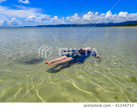 A woman floating in the clear and beautiful sea on a hot summer day. Blue sky, white clouds, mountains in the distance A woman floating in the clear and beautiful sea on a hot summer day. Blue sky, white clouds, mountains in the distance 81248713