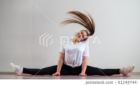 A young flexible fat woman sits in a transverse twine and waves her hair against a white background A young flexible fat woman sits in a transverse twine and waves her hair against a white background 81249744
