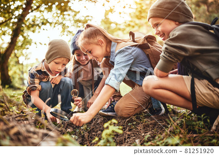 Happy school children boys and girls with backpacks making bonfire with magnifying glass in forest 81251920
