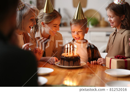 Happy little boy making wish and going to blow candles on cake while celebrating Birthday with big family 81252016