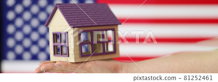 Small house with keys on hand against background of American flag Small house with keys on hand against background of American flag 81252461