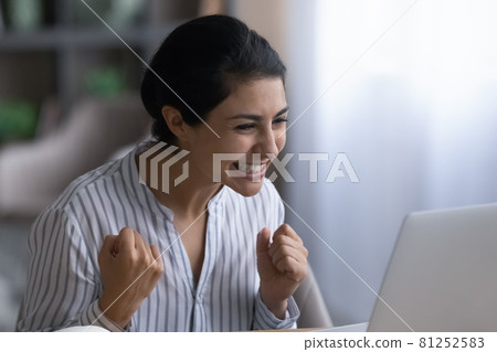 Overjoyed Indian woman triumphs reading good news on laptop 81252583