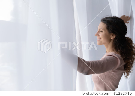 Young Latina woman open curtains looks out window feels happy Young Latina woman open curtains looks out window feels happy 81252710