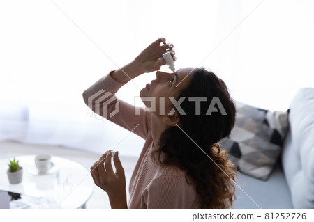 Young woman sit on sofa drips drops into eyes Young woman sit on sofa drips drops into eyes 81252726