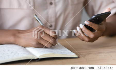 Close up of ethnic woman use cellphone write on paper Close up of ethnic woman use cellphone write on paper 81252738