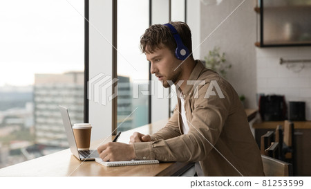 Man listens audio taking notes making assignment use laptop 81253599