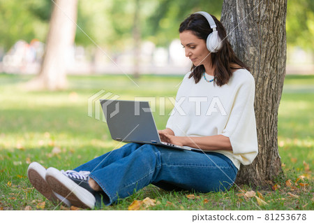 Portrait of a 40-years-old woman with laptop in city park during online vido call. Online working concept or concept of a distant online education. Portrait of a 40-years-old woman with laptop in city park during online vido call. Online working concept or concept of a distant online education. 81253678