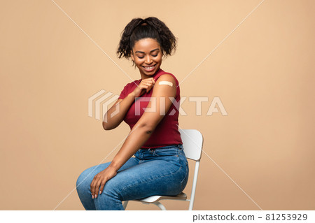 Black female patient showing shoulder with adhesive bandage after anti covid vaccine injection on beige background Black female patient showing shoulder with adhesive bandage after anti covid vaccine injection on beige background 81253929