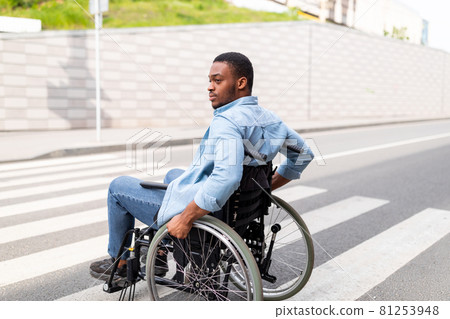 Quality of life and impairment. Millennial paraplegic black man in wheelchair using crosswalk outdoors in autumn Quality of life and impairment. Millennial paraplegic black man in wheelchair using crosswalk outdoors in autumn 81253948