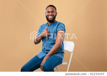 Black guy with band aid on his arm recommending anti covid vaccination, showing thumb up, receiving coronavirus vaccine 81254347
