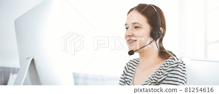 Casual dressed young woman using headset and computer while talking with customers online in sunny office. Call center Casual dressed young woman using headset and computer while talking with customers online in sunny office. Call center 81254616