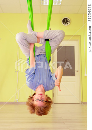 The child is doing yoga in a hammock in the hall. The child is doing yoga in a hammock in the hall. 81254928