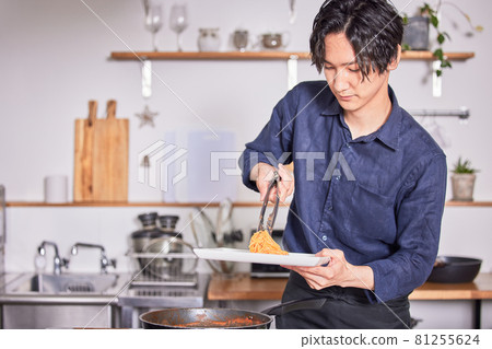 A young man in an apron serving pasta on a plate, a male cooking image A young man in an apron serving pasta on a plate, a male cooking image 81255624