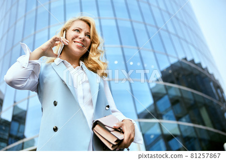 Happy manager talks by smartphone near glass business center. 81257867