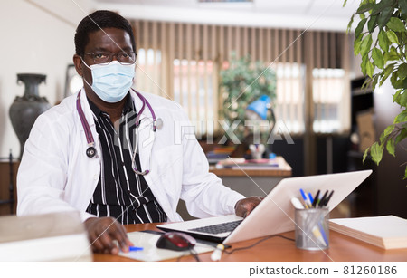 African american doctor in protective mask working with laptop 81260186