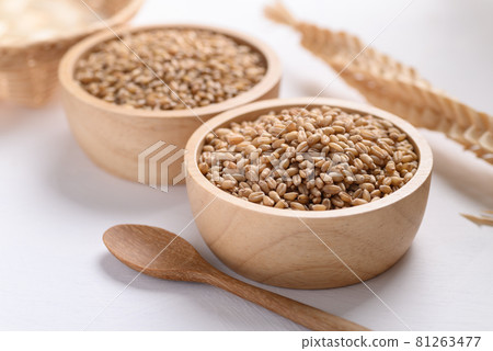 Wheat grain in a wooden bowl and spoon on white background 81263477