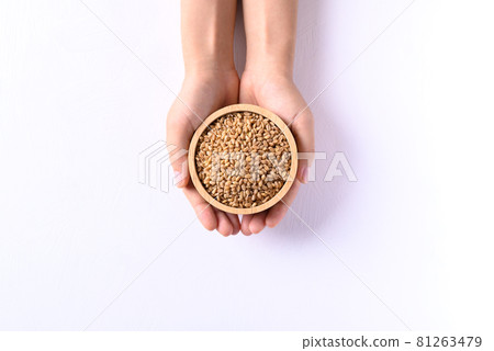 Wheat grain in a wooden bowl holding by hand on white background, Top view 81263479