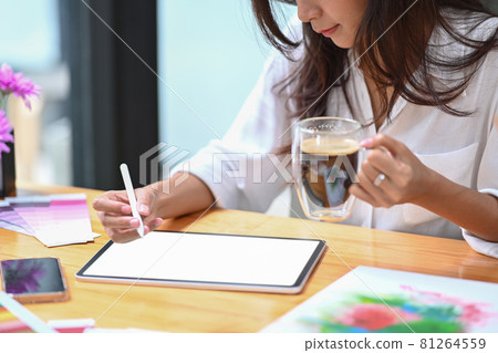 Cropped shot creative woman drinking coffee and drawing picture on digital tablet. Cropped shot creative woman drinking coffee and drawing picture on digital tablet. 81264559