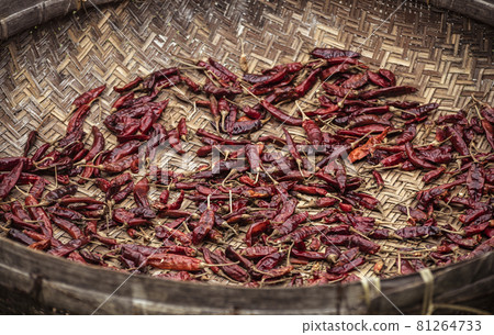 Red chili peppers drying out in the sun naturally, laying flat, and spreads thin out on a basket surface overhead view. Process of making hot and spicy dried chili powder. Red chili peppers drying out in the sun naturally, laying flat, and spreads thin out on a basket surface overhead view. Process of making hot and spicy dried chili powder. 81264733