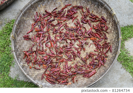 Red chili peppers drying out in the sun naturally, laying flat, and spreads thin out on a basket surface close-up view. Process of making hot and spicy dried chili powder. 81264734