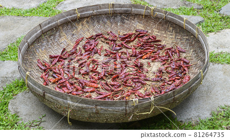 Red chili peppers drying out in the sun naturally, laying flat, and spreads thin out on a basket surface. Process of making hot and spicy dried chili powder. Red chili peppers drying out in the sun naturally, laying flat, and spreads thin out on a basket surface. Process of making hot and spicy dried chili powder. 81264735