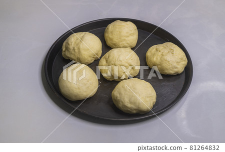 Flour dough balls resting on an oily surface on the round pizza plate. Dough balls have perfectly risen. Hand kneaded the dough for making homemade pastry buns to bake in the oven. Flour dough balls resting on an oily surface on the round pizza plate. Dough balls have perfectly risen. Hand kneaded the dough for making homemade pastry buns to bake in the oven. 81264832