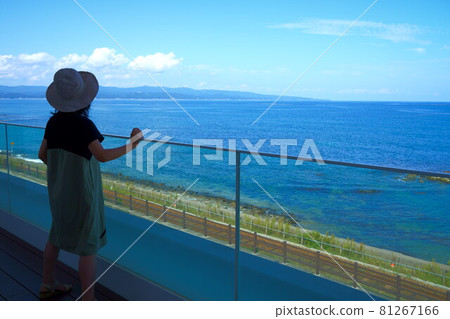 Full body behind a woman looking at the coastline on the roadside station Amahari deck 81267166