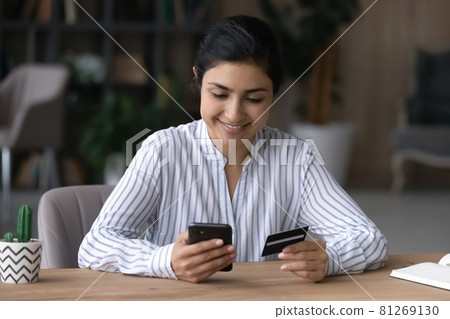 Smiling Indian woman shopping online on cell 81269130