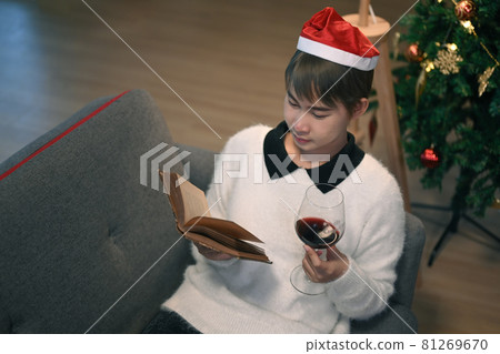 Young woman wears Christmas hat drinking red from glass sitting on couch near Christmas tree and celebrating winter holiday in quarantine isolation pandemic. Young woman wears Christmas hat drinking red from glass sitting on couch near Christmas tree and celebrating winter holiday in quarantine isolation pandemic. 81269670