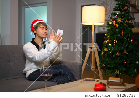 Happy young woman wears santa hat talking meeting friends on video call celebrating in holiday distance online together on mobile phone at home. 81269735