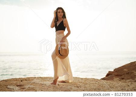 Young stylish woman standing on cliff at the sea at sunset 81270353