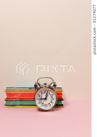 A stack of colorful notebooks and an alarm clock on the table. A vertical frame with space. Pastel colors. A stack of colorful notebooks and an alarm clock on the table. A vertical frame with space. Pastel colors. 81274077