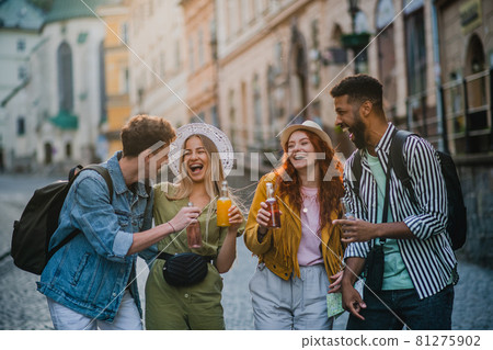 Front view of group of happy young people with drinks outdoors on street on town trip, laughing. Front view of group of happy young people with drinks outdoors on street on town trip, laughing. 81275902
