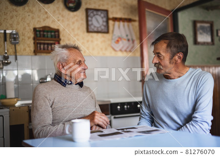 Portrait of man with elderly father sitting at the table indoors at home, talking. Portrait of man with elderly father sitting at the table indoors at home, talking. 81276070